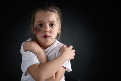 Photo of Little girl with bruises on face against dark background, space for text. Domestic violence victim