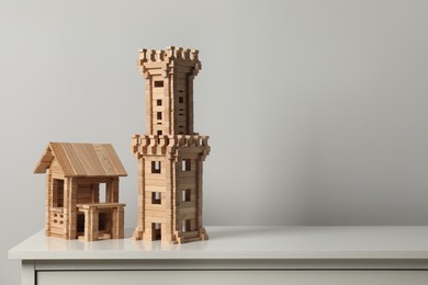 Photo of Wooden tower and house on chest of drawers near light grey wall, space for text. Children's toys