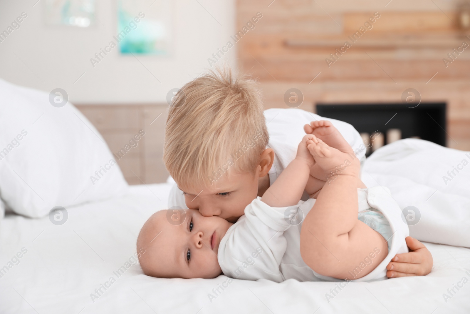 Photo of Cute boy kissing his little sister on bed at home