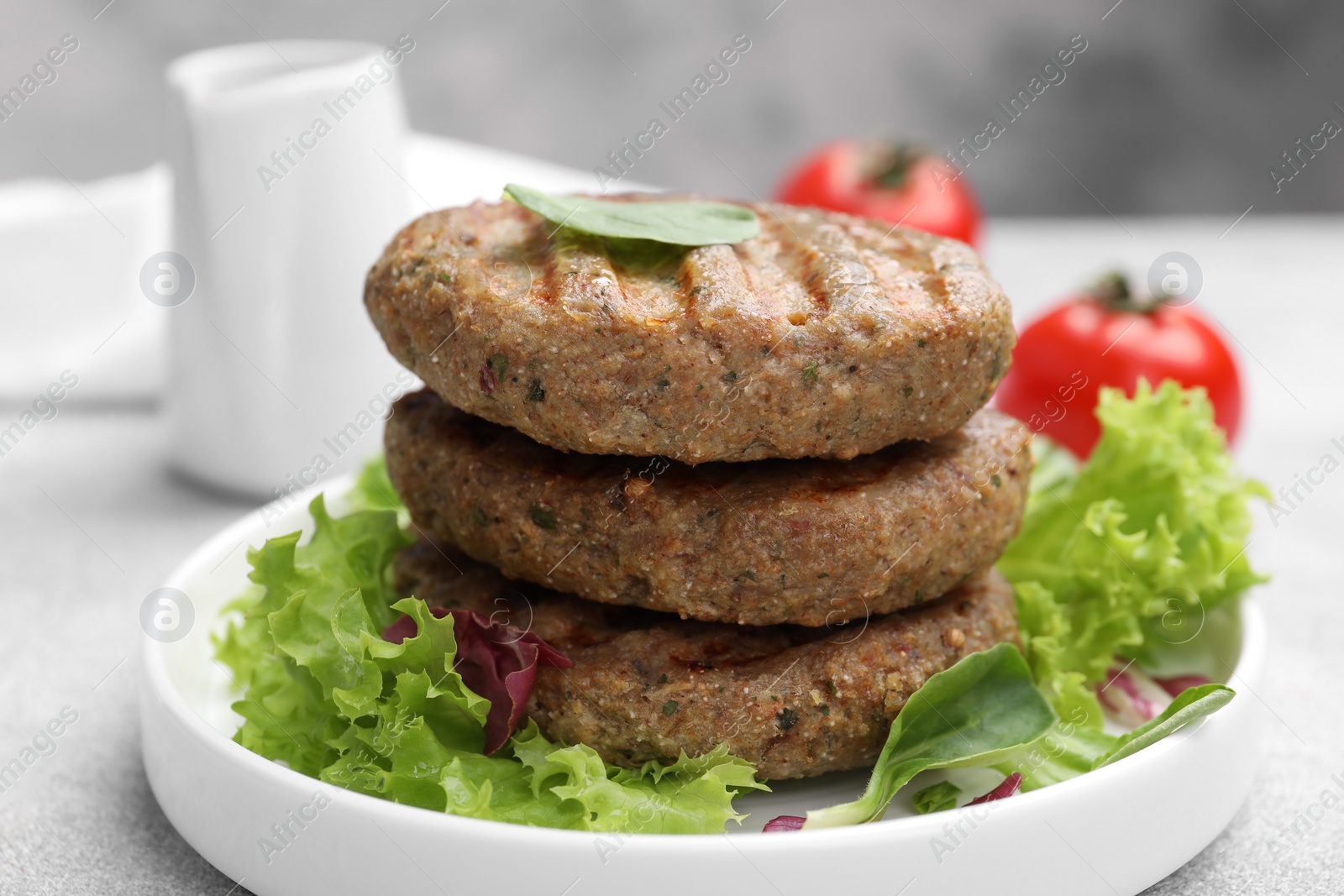 Photo of Delicious grilled vegan cutlets, lettuce and spinach on light grey table, closeup