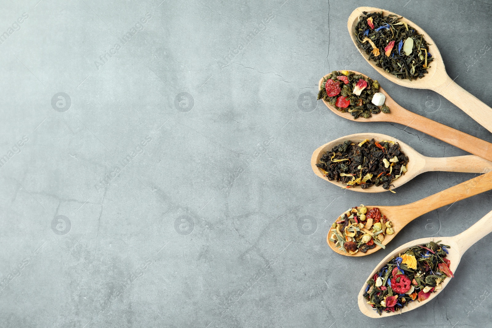 Photo of Different kinds of dry herbal tea in wooden spoons on light grey table, flat lay. Space for text