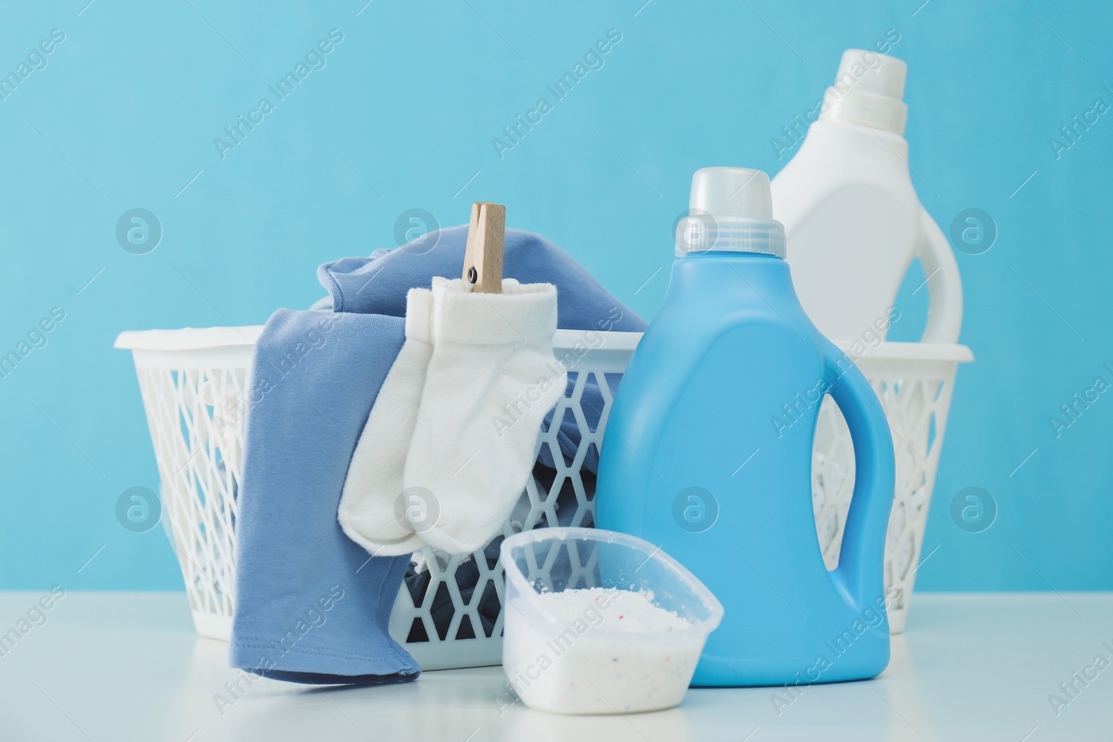 Photo of Detergents and children's clothes on white table near light blue wall