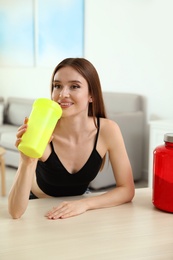 Photo of Young woman drinking protein shake at table indoors