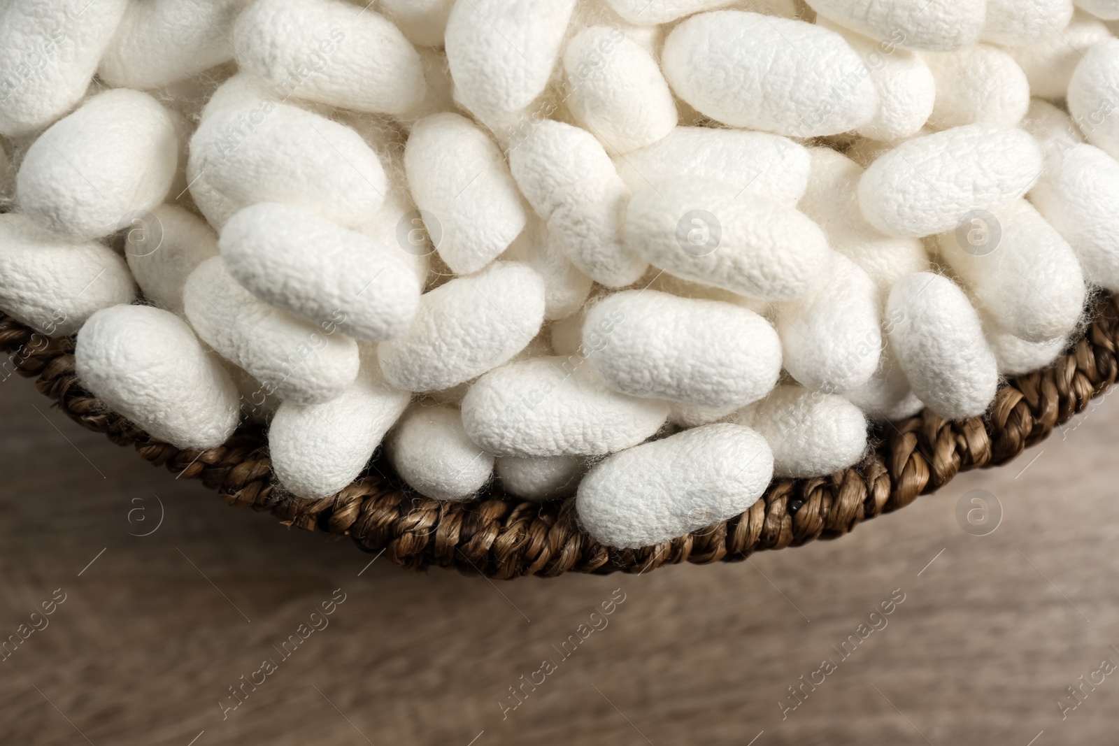 Photo of White silk cocoons in bowl on wooden table, closeup