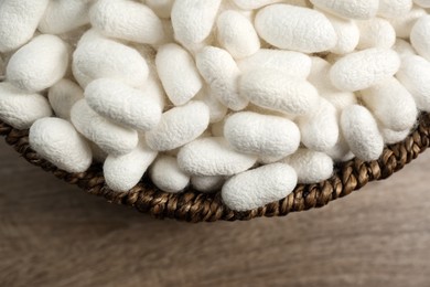 White silk cocoons in bowl on wooden table, closeup