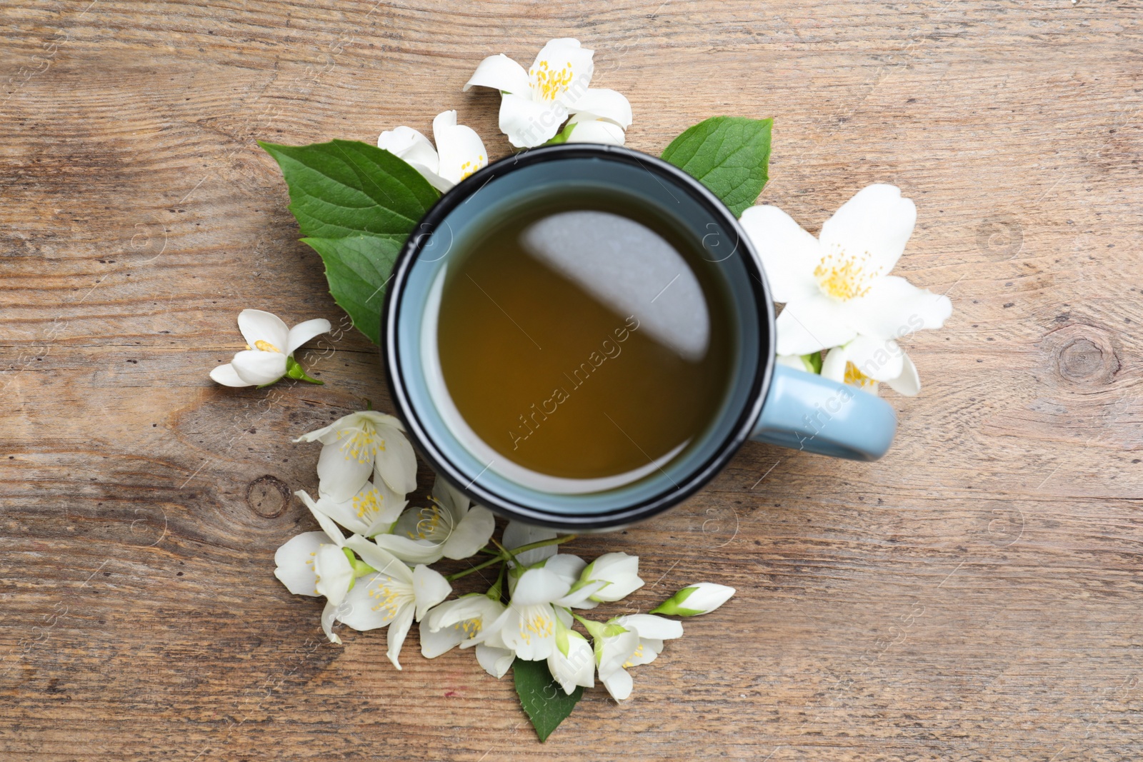 Photo of Cup of tea and fresh jasmine flowers on wooden table, flat lay