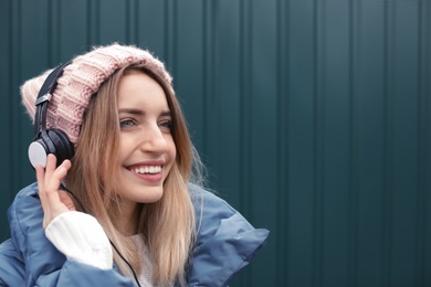 Photo of Young woman with headphones listening to music near color wall. Space for text