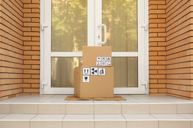 Photo of Cardboard boxes with different packaging symbols on door mat near entrance. Parcel delivery