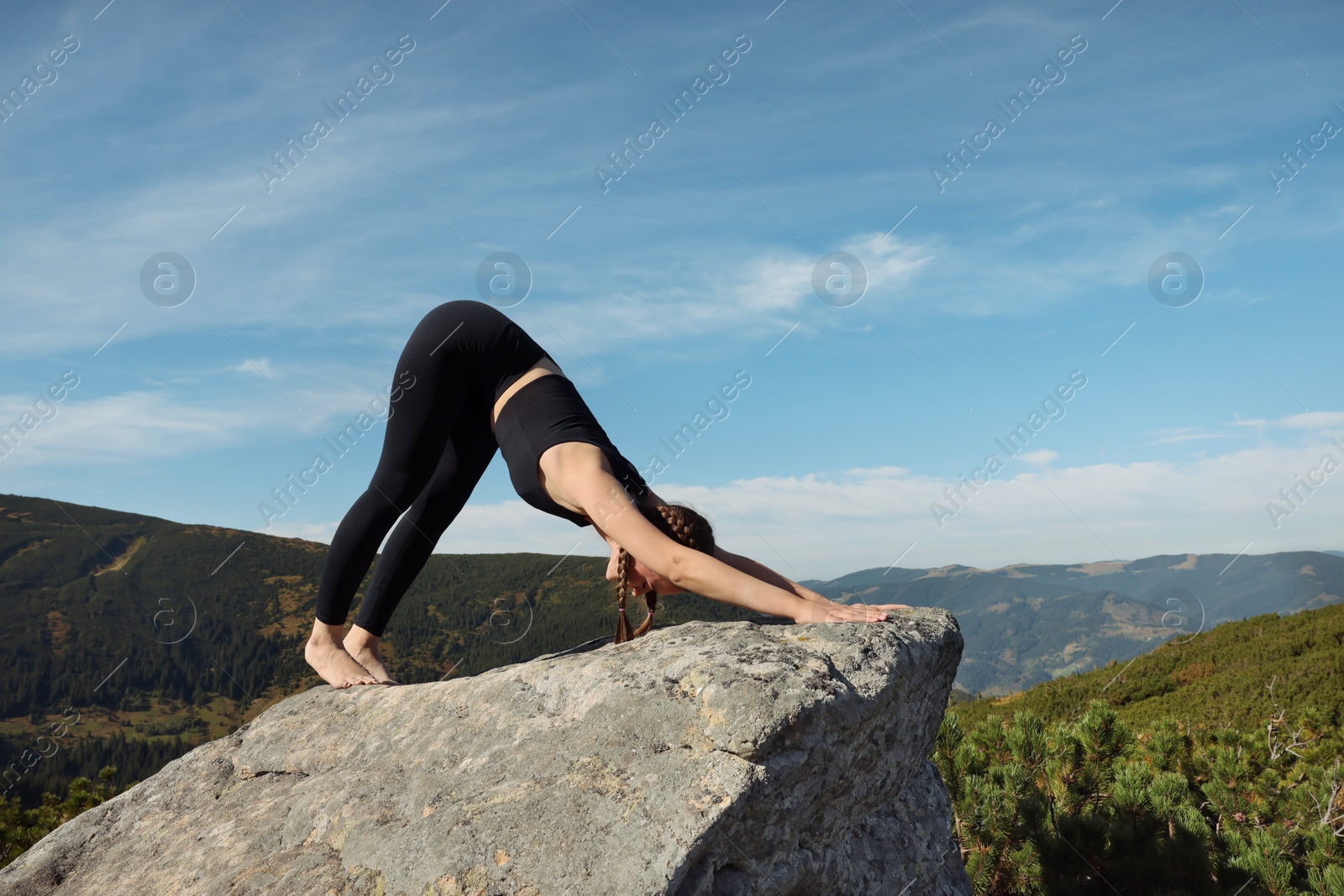 Photo of Beautiful young woman practicing yoga on rock in mountains