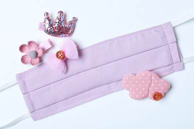 Homemade protective mask and adorable girly hair clips on white background, flat lay. Sewing for child