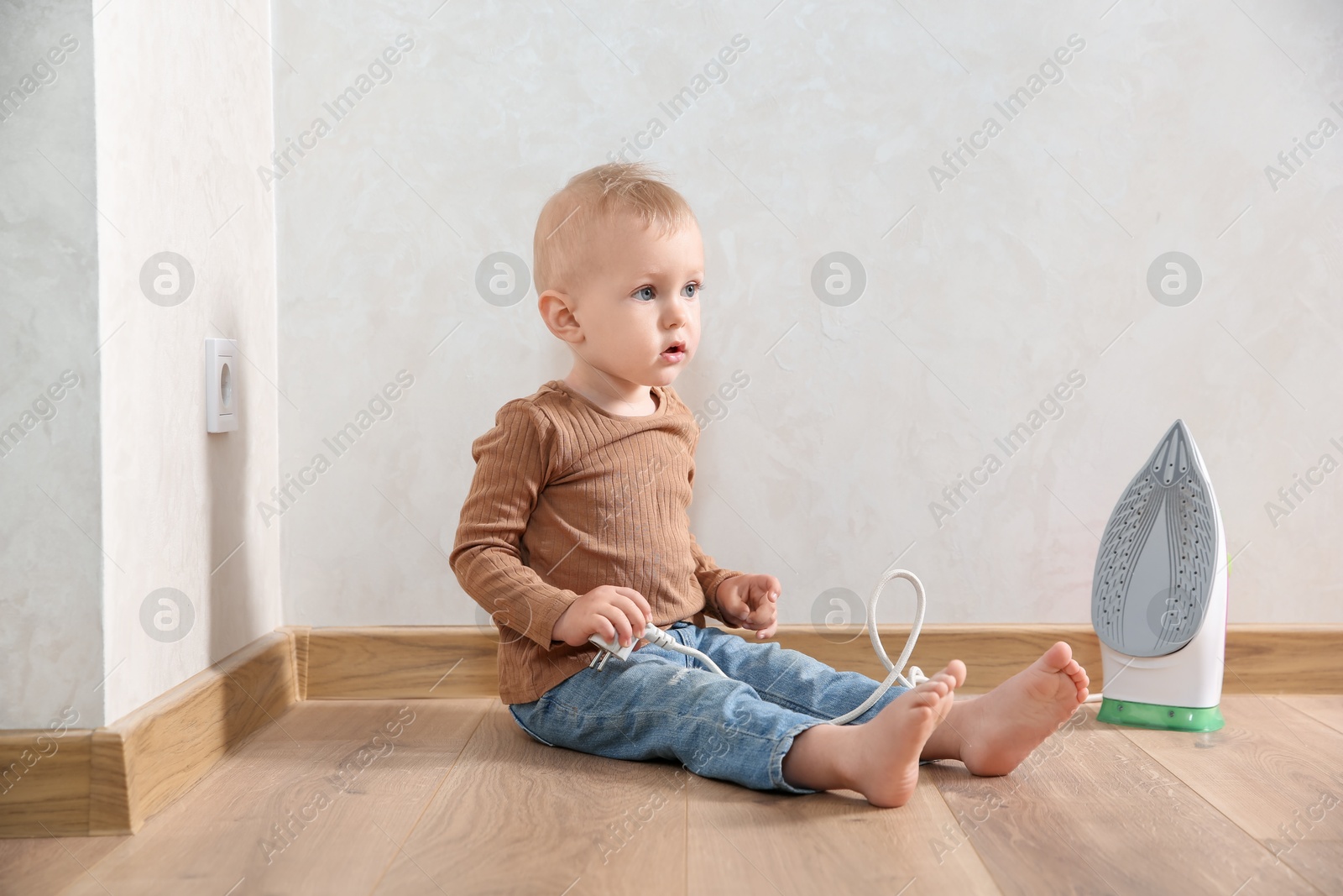 Photo of Little child playing with iron plug near electrical socket at home. Dangerous situation