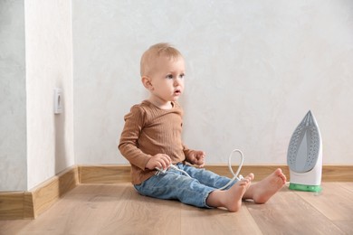 Photo of Little child playing with iron plug near electrical socket at home. Dangerous situation