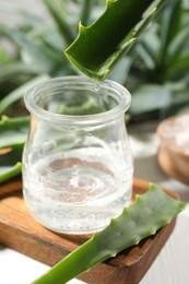 Dripping aloe vera gel from leaf into jar at white table, closeup