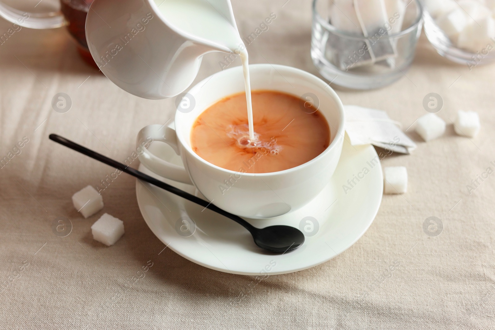 Photo of Pouring milk into cup with tea on light table, closeup