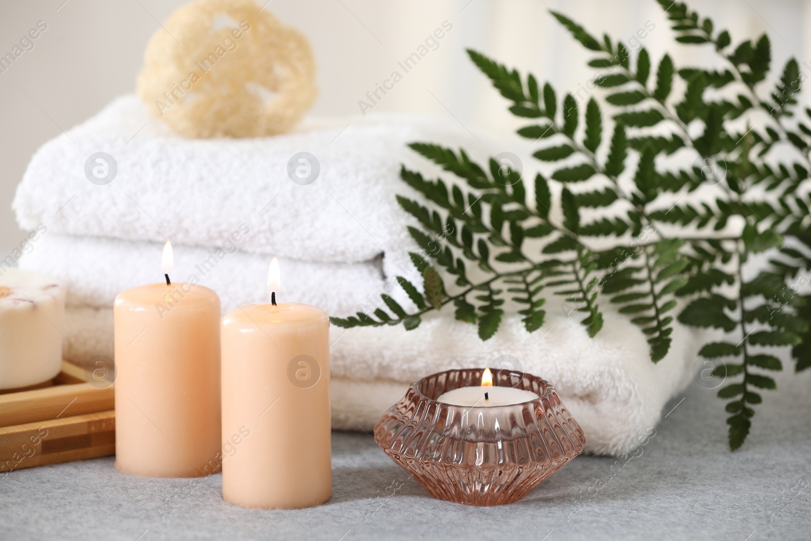 Photo of Spa composition. Burning candles, towels and loofah on soft grey surface