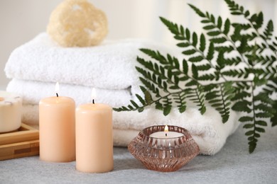 Photo of Spa composition. Burning candles, towels and loofah on soft grey surface