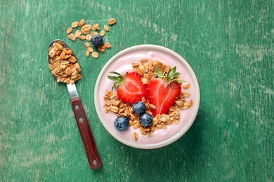 Photo of Bowl with yogurt, berries and granola on wooden background, top view
