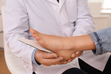 Photo of Male orthopedist fitting insole on patient's foot in clinic, closeup