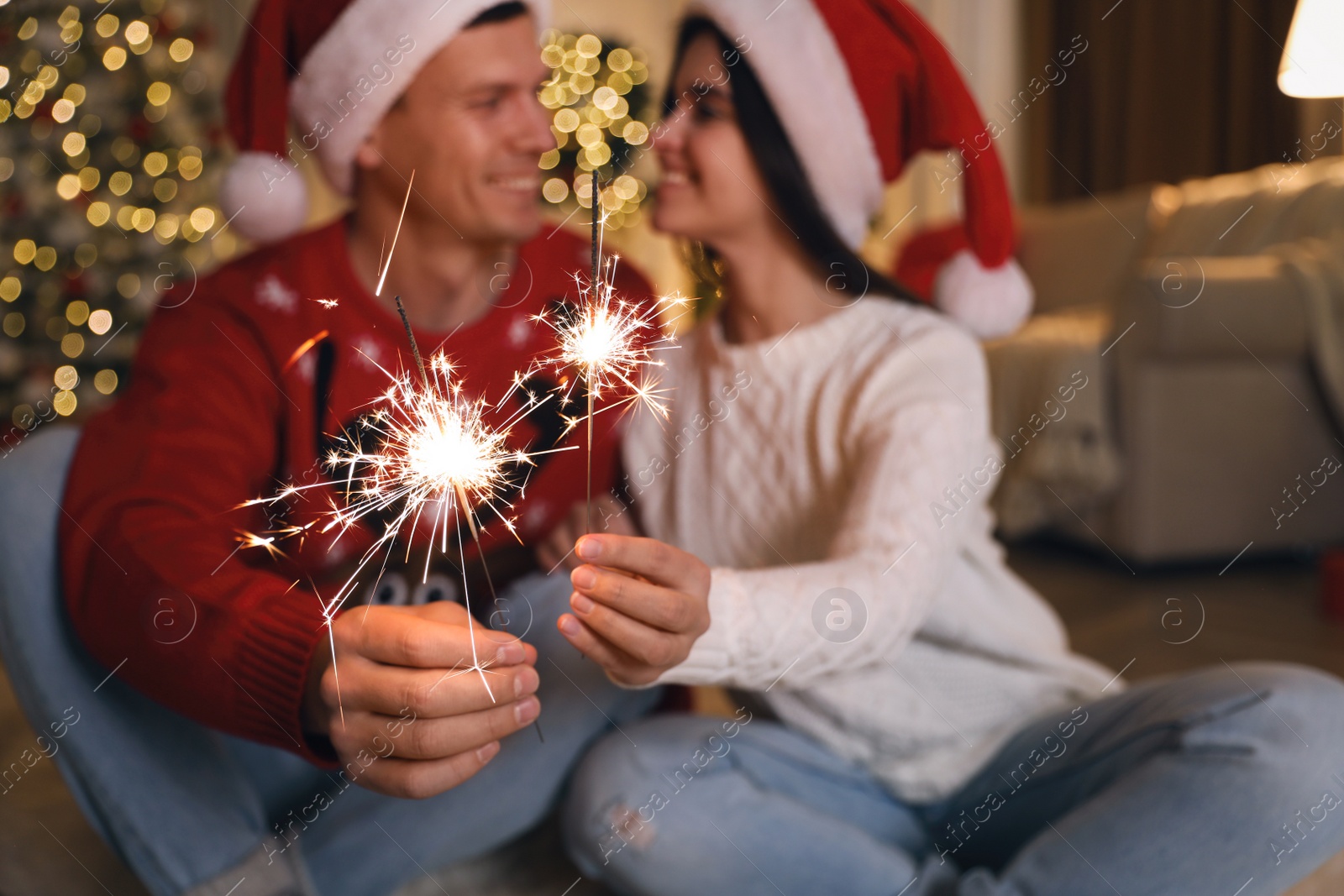 Photo of Couple holding sparkles in room decorated for Christmas, focus on fireworks