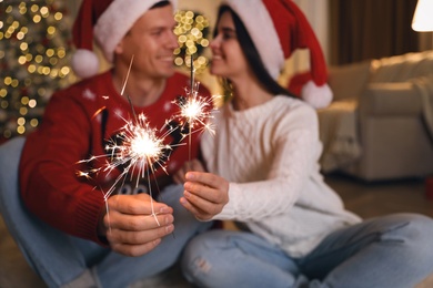 Couple holding sparkles in room decorated for Christmas, focus on fireworks