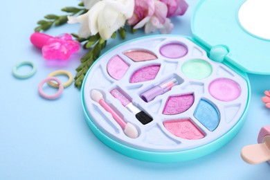 Photo of Decorative cosmetics for kids. Eye shadow palette, accessories and flowers on light blue background, closeup