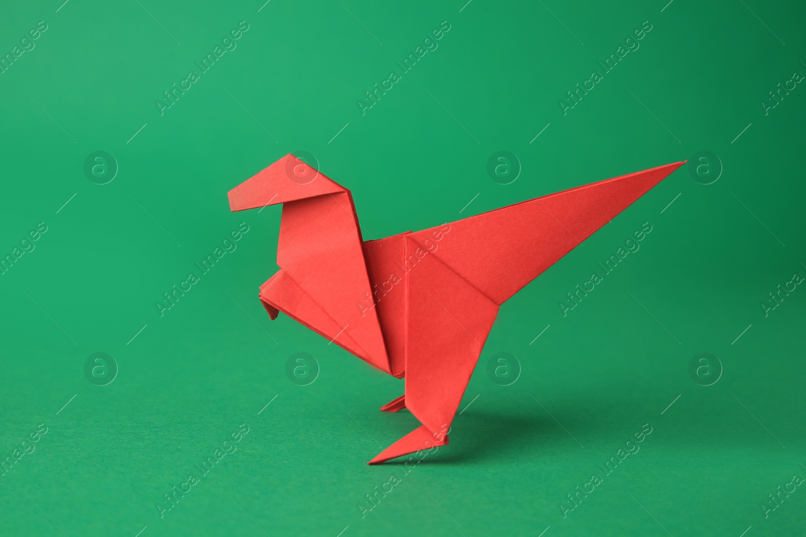 Photo of Origami art. Handmade red paper dinosaur on green background