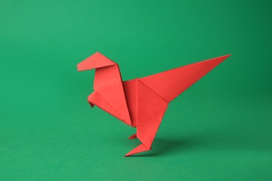 Photo of Origami art. Handmade red paper dinosaur on green background