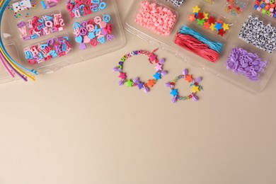 Photo of Handmade jewelry kit for kids. Colorful beads, wristbands and bracelets on beige background, flat lay. Space for text