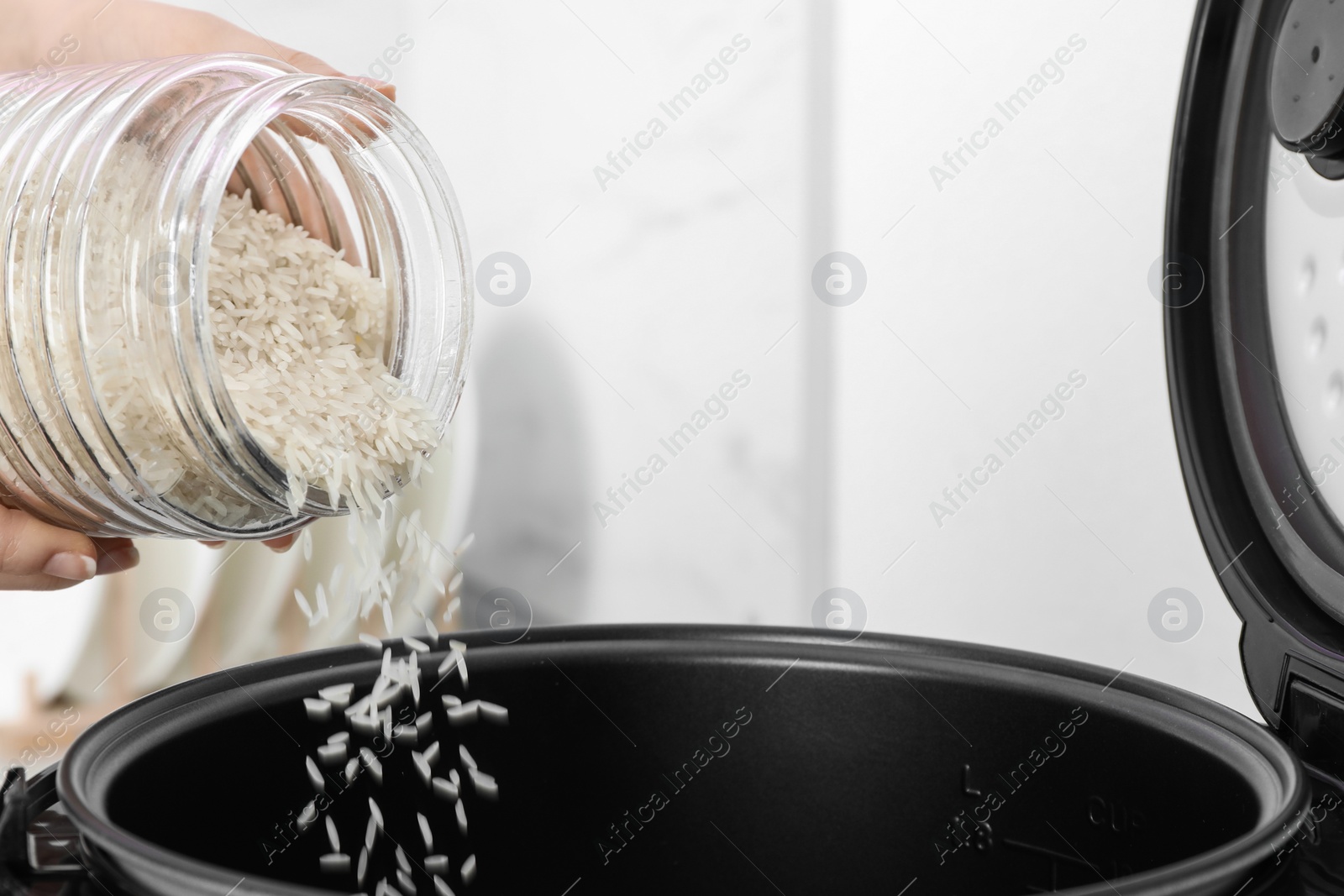 Photo of Woman pouring rice from jar into cooker in kitchen, closeup