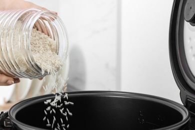 Photo of Woman pouring rice from jar into cooker in kitchen, closeup