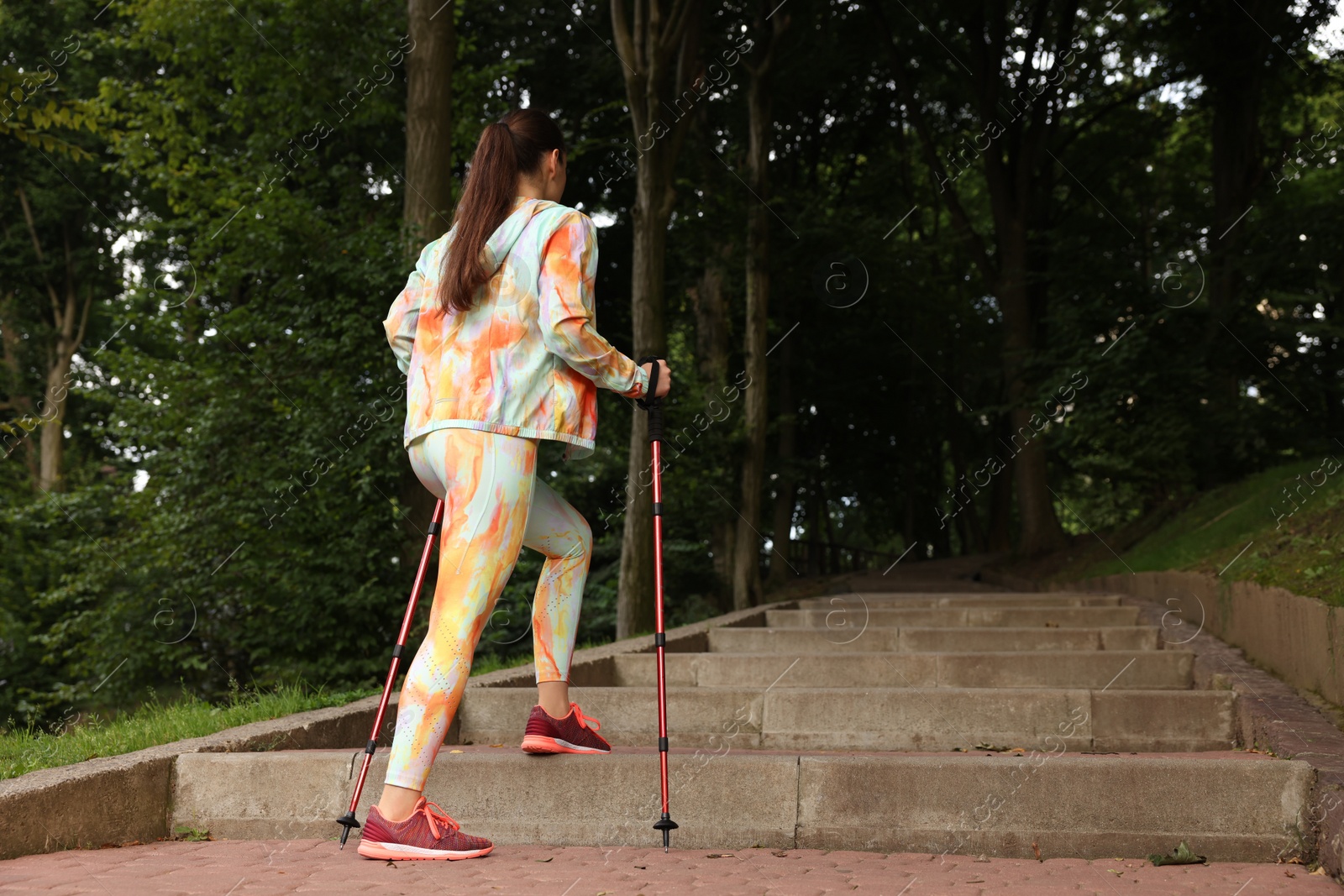 Photo of Young woman practicing Nordic walking with poles on steps outdoors, low angle view. Space for text