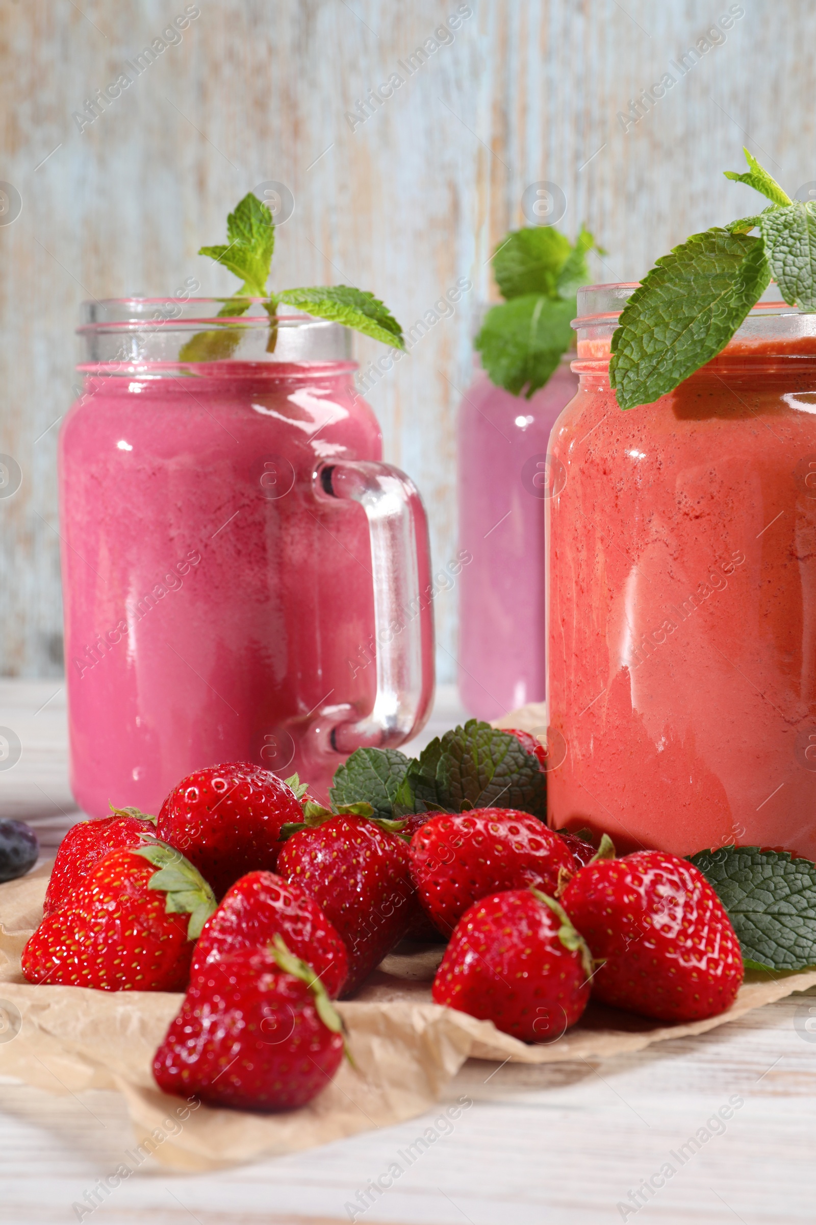 Photo of Mason jars of different berry smoothies and fresh ingredients on white wooden table, closeup