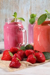 Mason jars of different berry smoothies and fresh ingredients on white wooden table, closeup