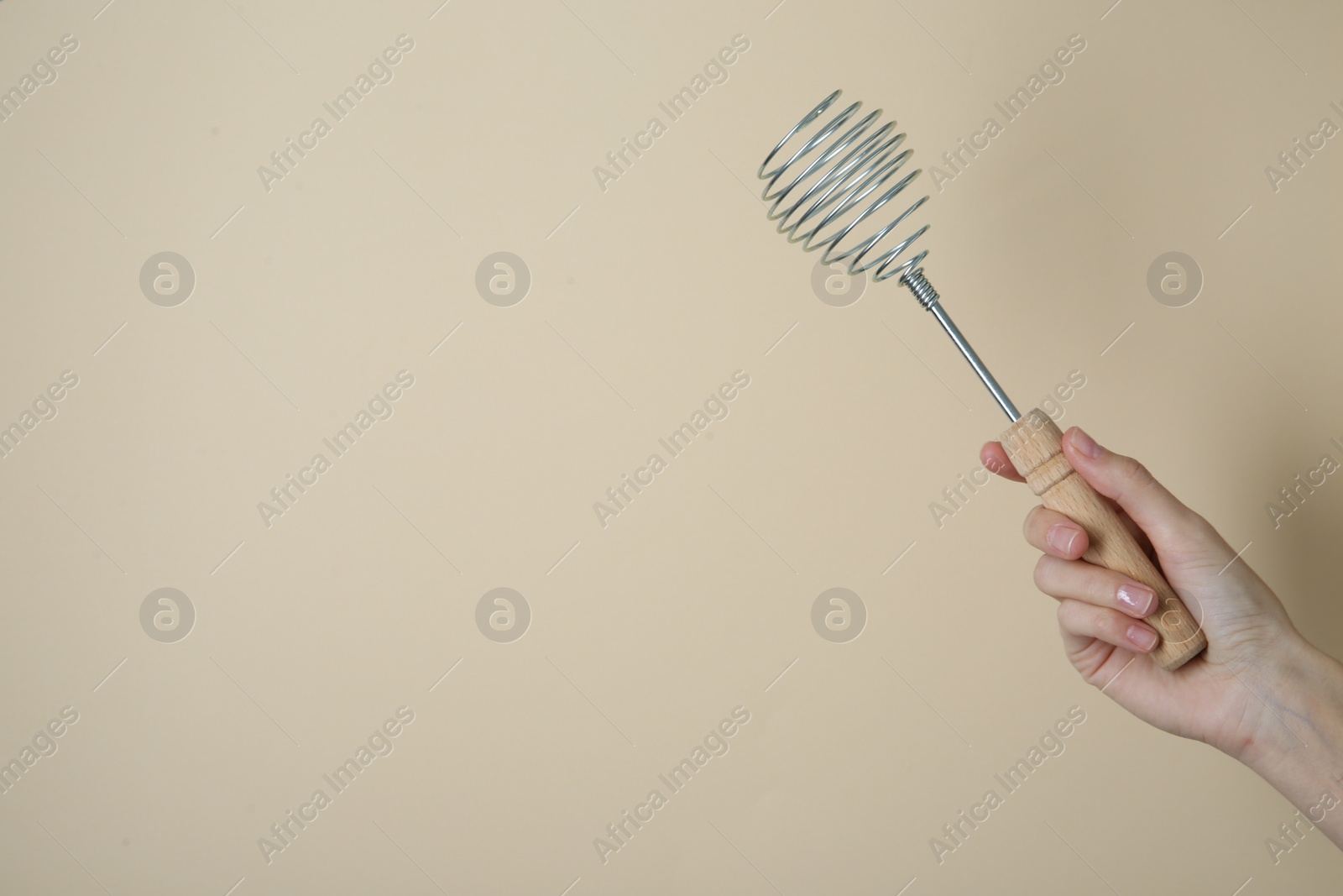 Photo of Woman holding metal whisk on beige background, closeup. Space for text