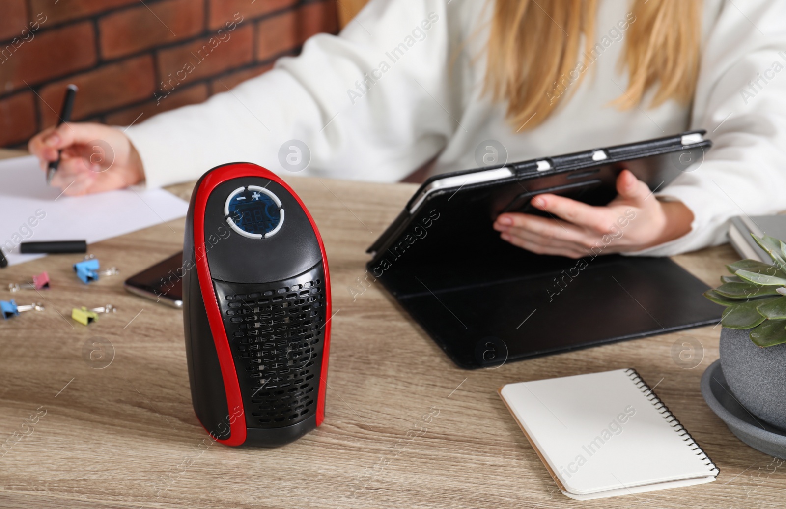 Photo of Compact electric heater on wooden table near woman indoors, closeup