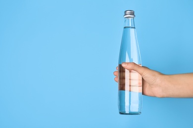 Photo of Woman holding glass bottle with water on light blue background, closeup. Space for text