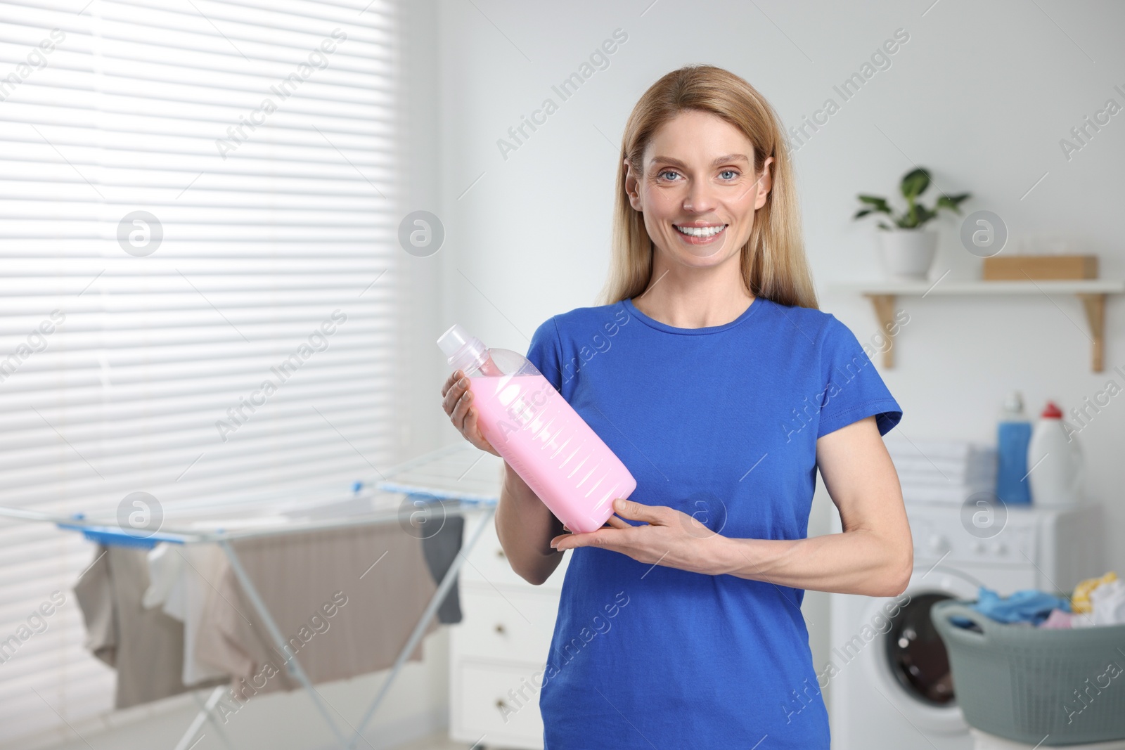 Photo of Woman holding fabric softener in bathroom, space for text