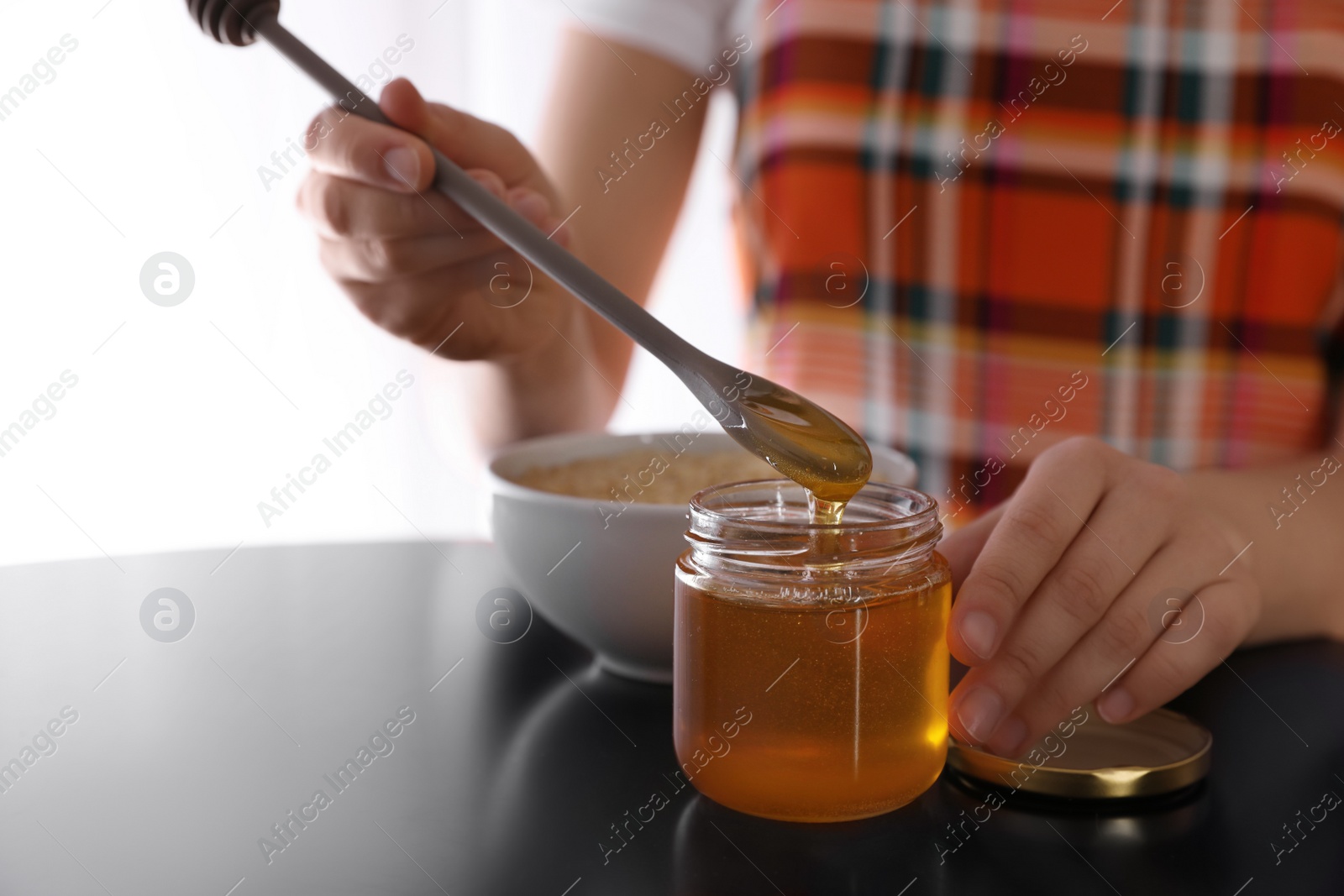 Photo of Woman with honey and spoon at black table, closeup