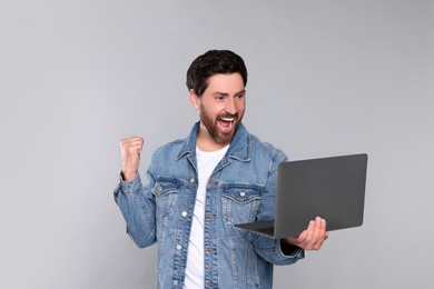 Emotional man with laptop on light grey background