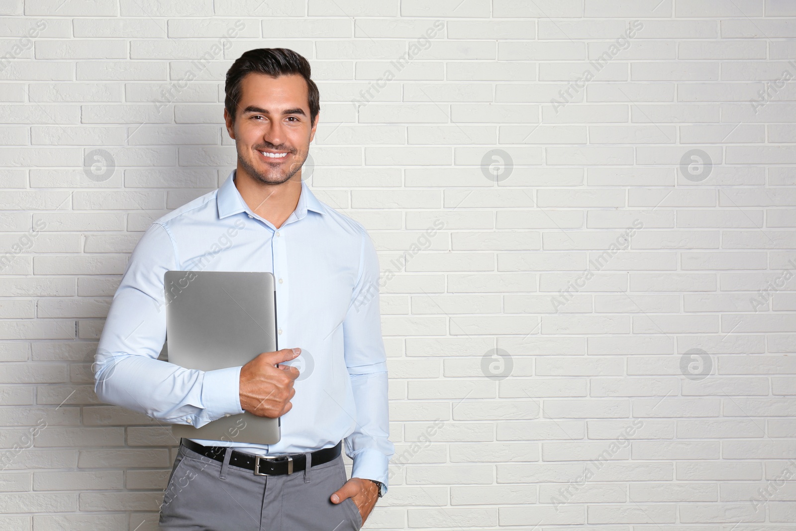 Photo of Young male teacher with laptop near brick wall. Space for text