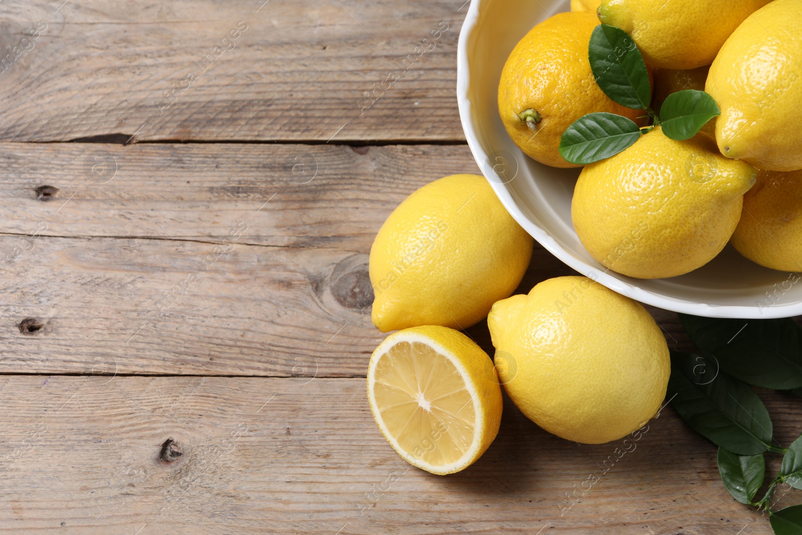 Photo of Fresh lemons and green leaves on wooden table. Space for text