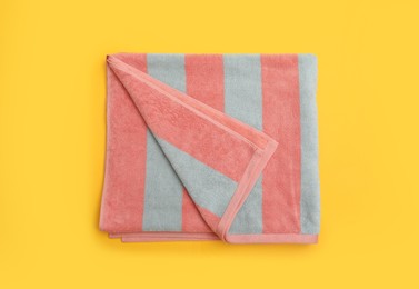 Folded striped beach towel on yellow background, top view