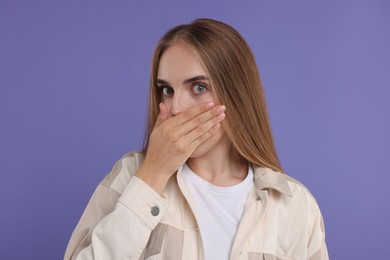 Photo of Embarrassed woman covering mouth with hand on violet background