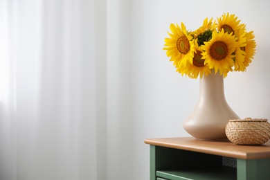 Photo of Bouquet of beautiful sunflowers and wicker basket on table indoors. Space for text