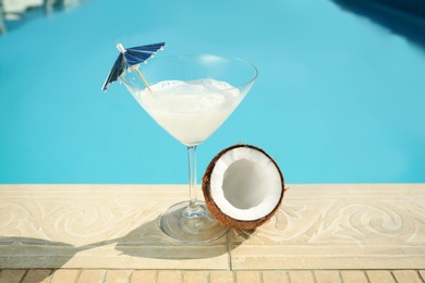 Photo of Tasty refreshing cocktail and coconut on edge of swimming pool. Party items