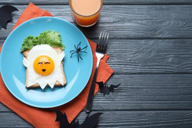 Halloween themed breakfast served on black wooden table, flat lay and space for text. Tasty toast with fried egg in shape of ghost