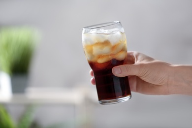 Photo of Woman holding glass of cola with ice on blurred background, closeup. Space for text
