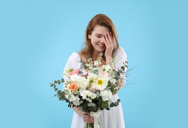 Beautiful woman with bouquet of flowers on light blue background