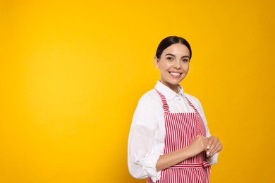 Photo of Young woman in red striped apron on yellow background, space for text