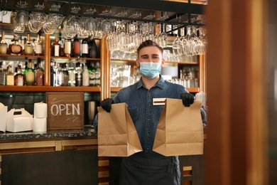 Photo of Waiter with packed takeout orders in restaurant. Food service during coronavirus quarantine